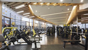 Un gimnasio amplio con diversos equipos de ejercicio, amplias ventanas y un diseño moderno en el techo.