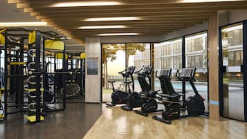 Un gimnasio con equipo de ejercicio, ventanas amplias y vistas a un edificio cercano.