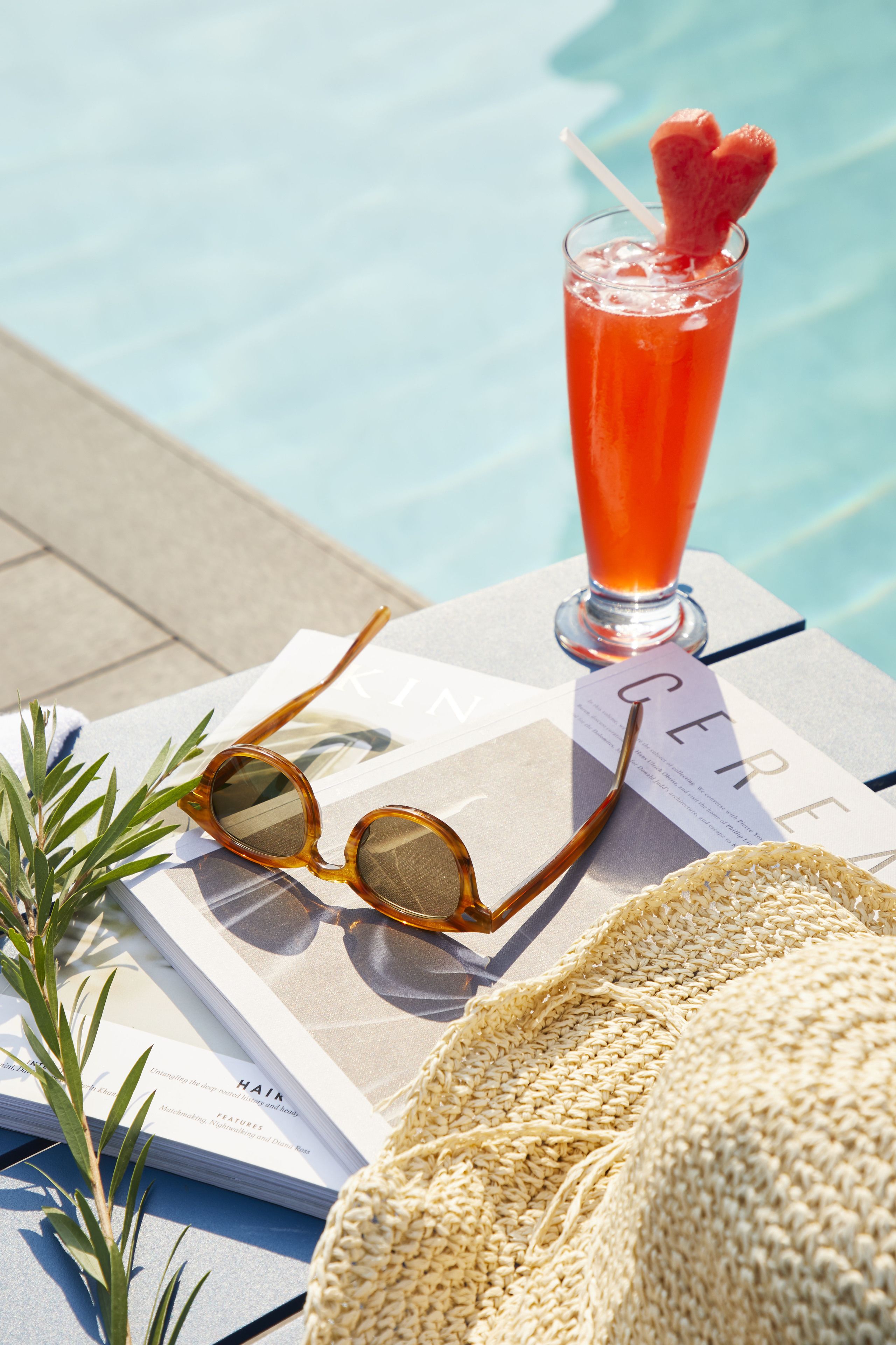 Un cadre agréable au bord de la piscine, avec une boisson, des lunettes de soleil et un magazine.