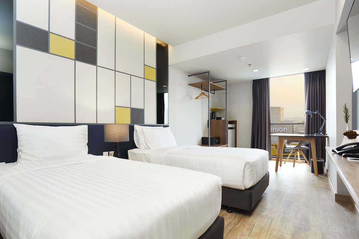 Een hotelkamer met twee bedden, een bureau en uitzicht op de stad.