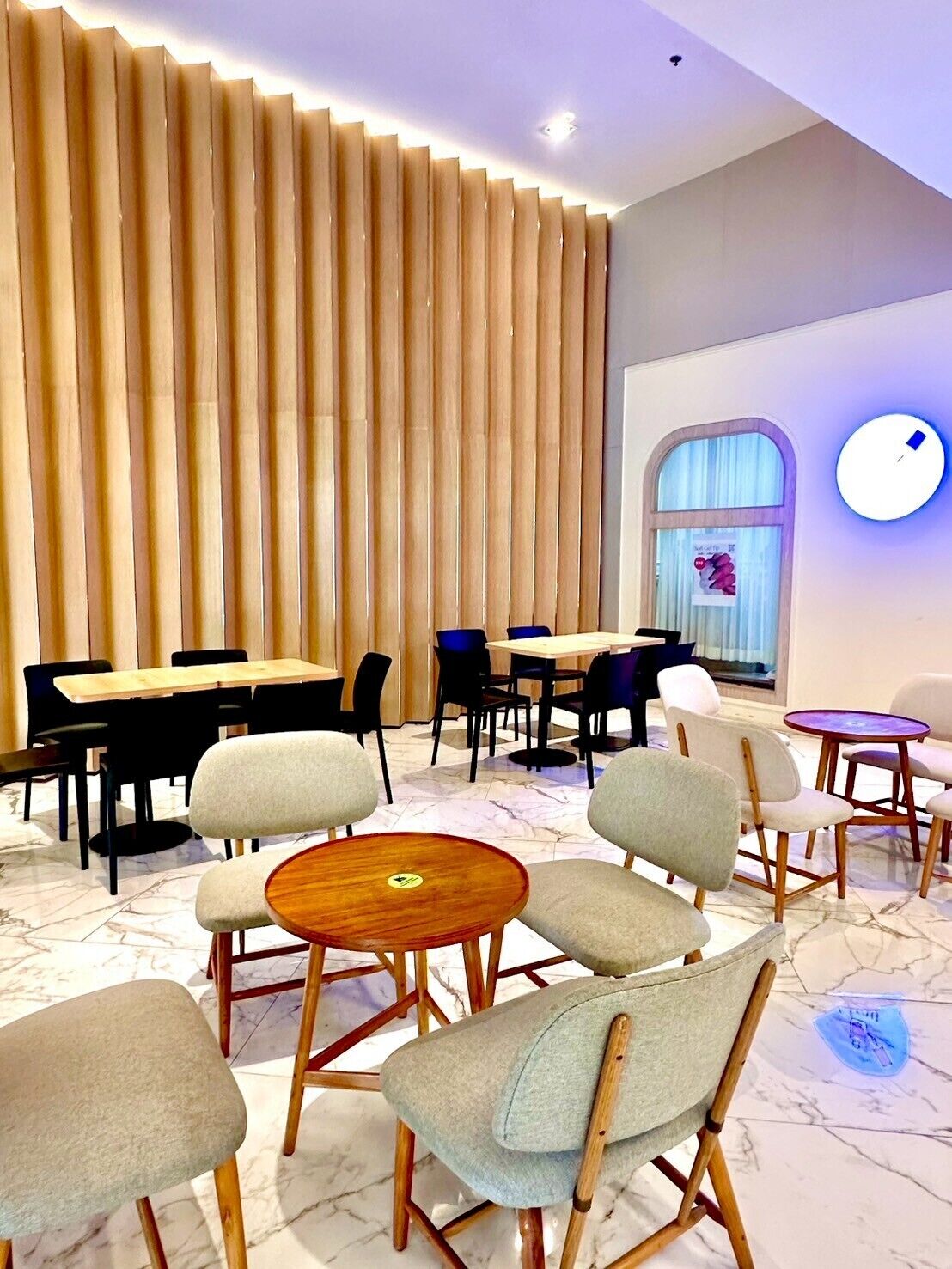 A modern dining area with wooden slats, round tables, and cushioned chairs.