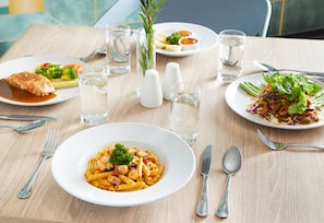Een eettafel met borden pasta, salade en andere gerechten, samen met bestek en glazen.