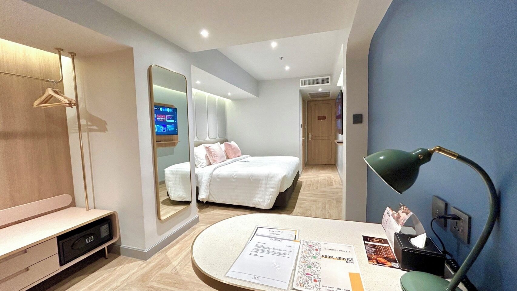 Une chambre d’hôtel moderne équipée d’un lit, d’une table de chevet, d’un miroir et d’un bureau avec une lampe.
