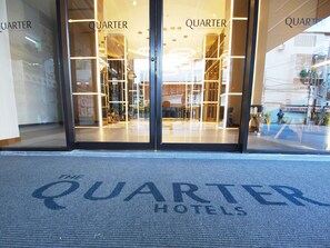 De ingang van The Quarter Hotel met glazen deuren en een zichtbaar interieur.