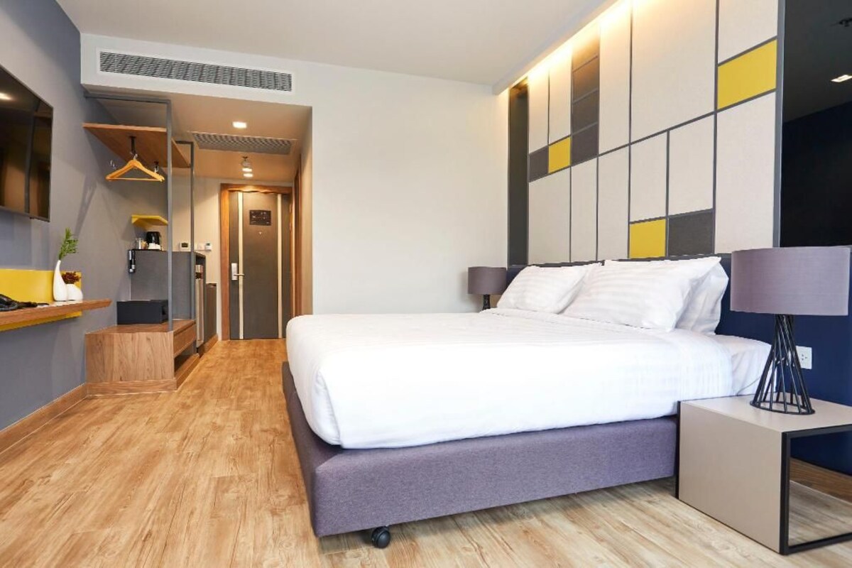 Habitación de hotel moderna con una cama grande, mesitas de noche, un armario y un pasillo que conduce a un baño.