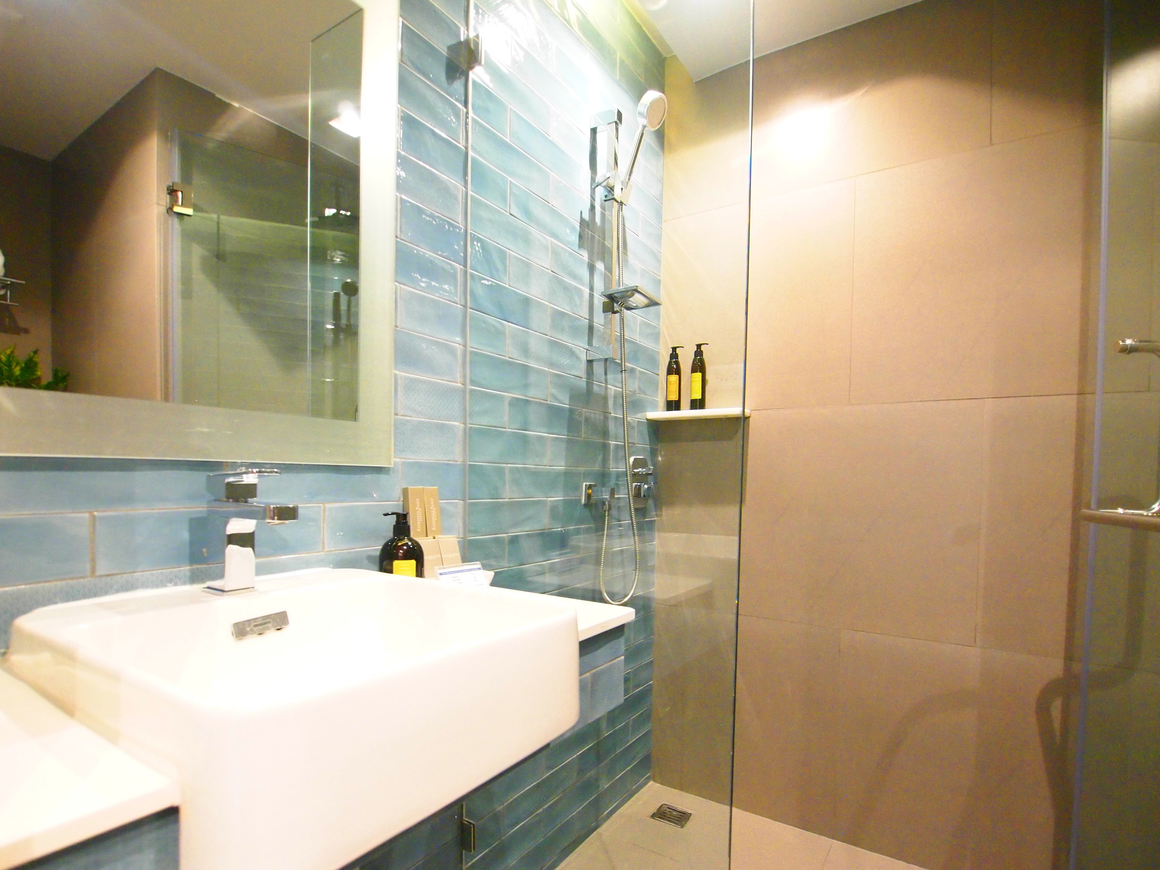 A modern bathroom with a white sink, blue-tiled walls, a glass shower enclosure, and a mirror above the sink.