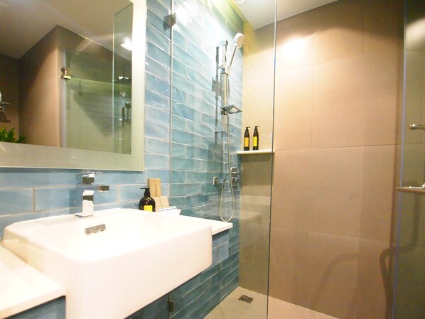Un baño moderno con un lavamanos blanco, paredes con azulejos azules, cabina de ducha de cristal y un espejo sobre el lavamanos.