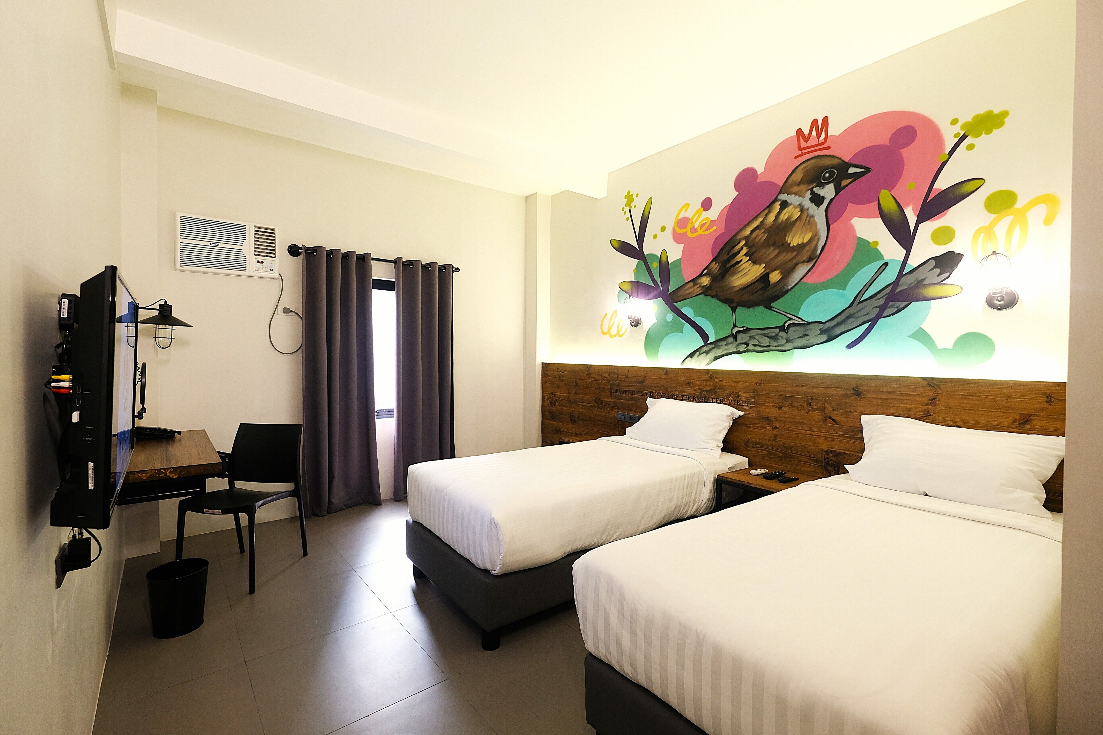A hotel room with two beds, a desk, a chair, a TV, and a wall mural.
