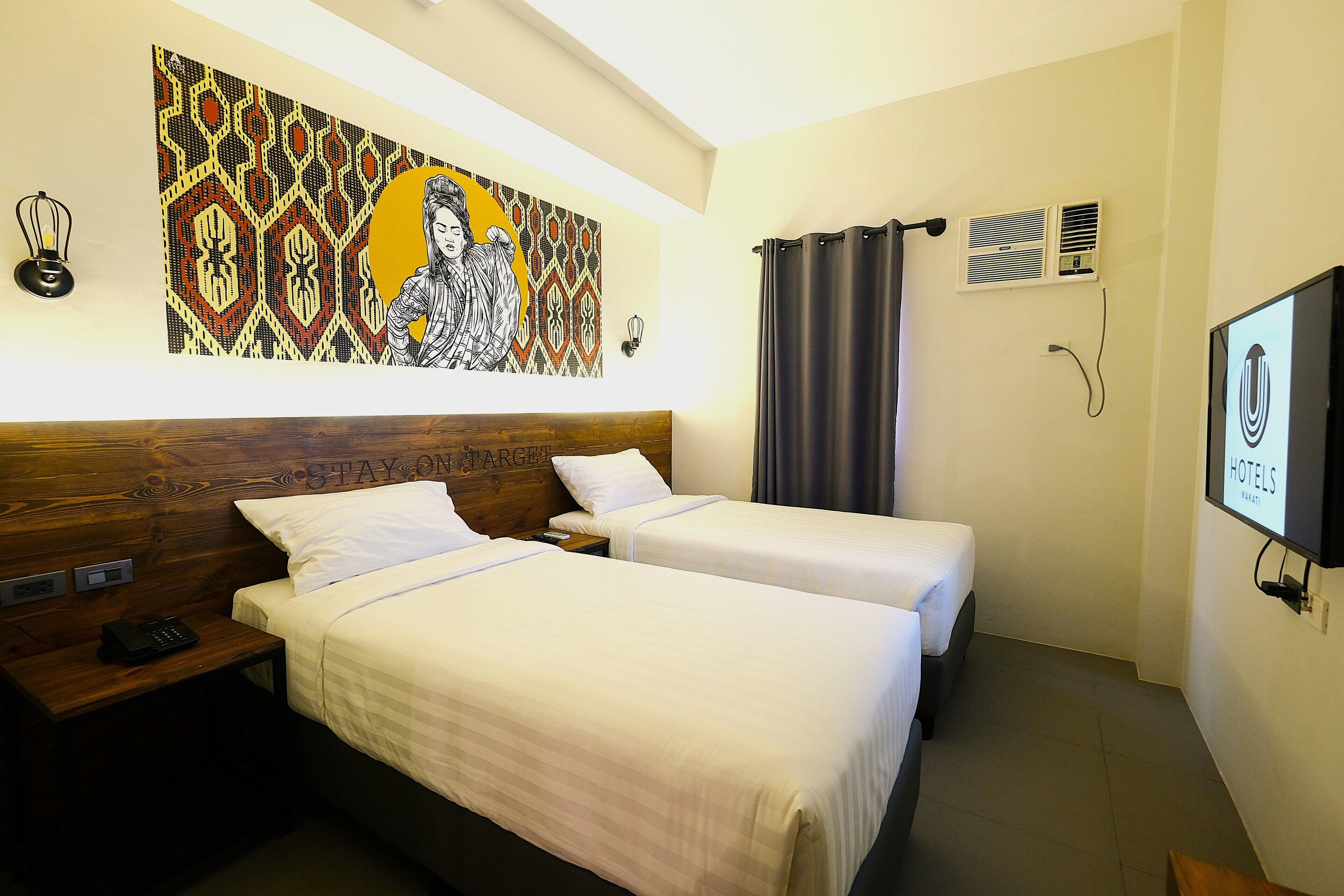A hotel room with two beds, a wooden headboard, a large wall painting, a television, and a curtain.