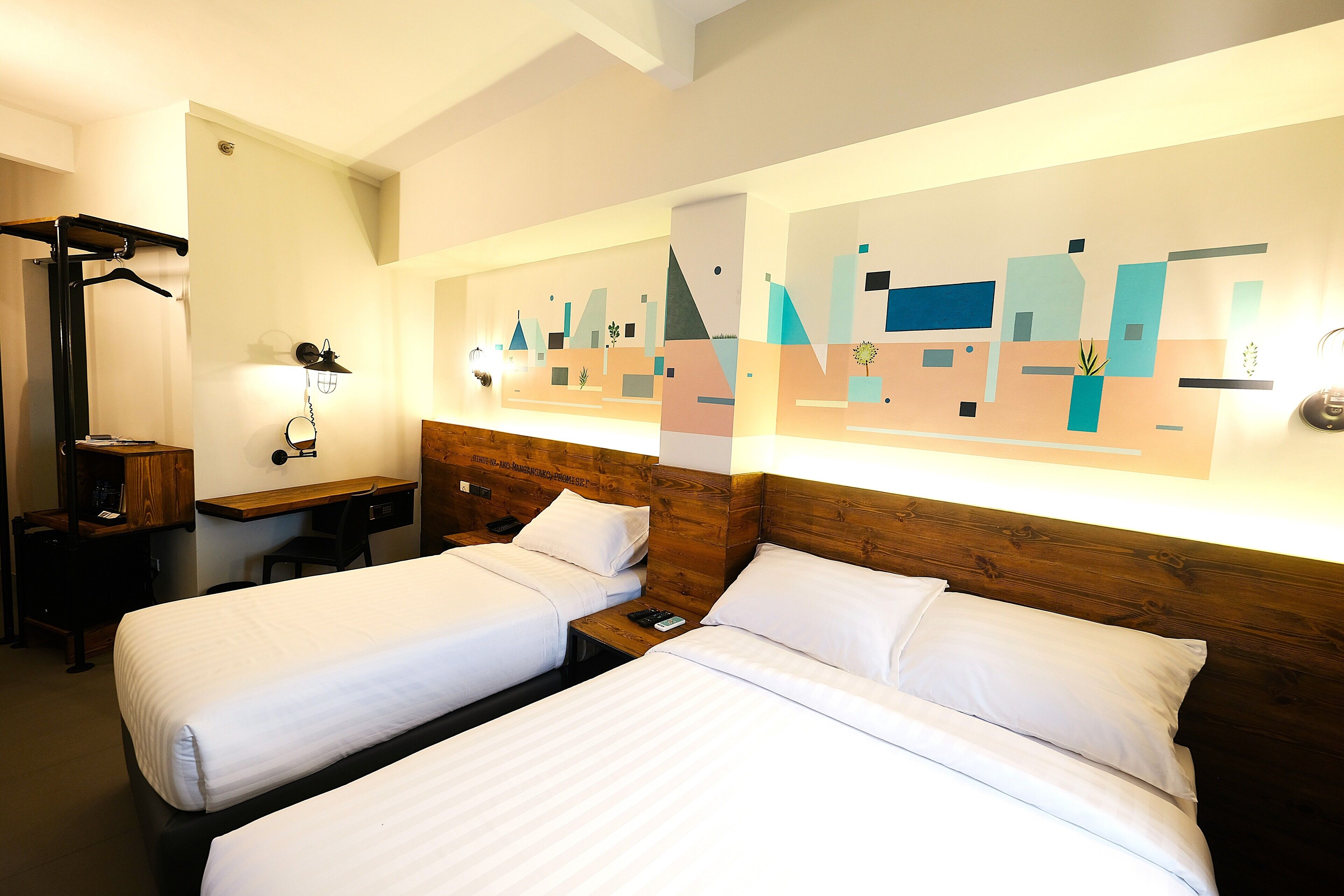Una habitación de hotel con dos camas, un cabecero de madera, un escritorio y una obra de arte en la pared.