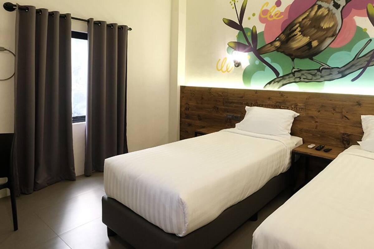 A hotel room with two beds, a wooden headboard, a wall mural, and a window with curtains.
