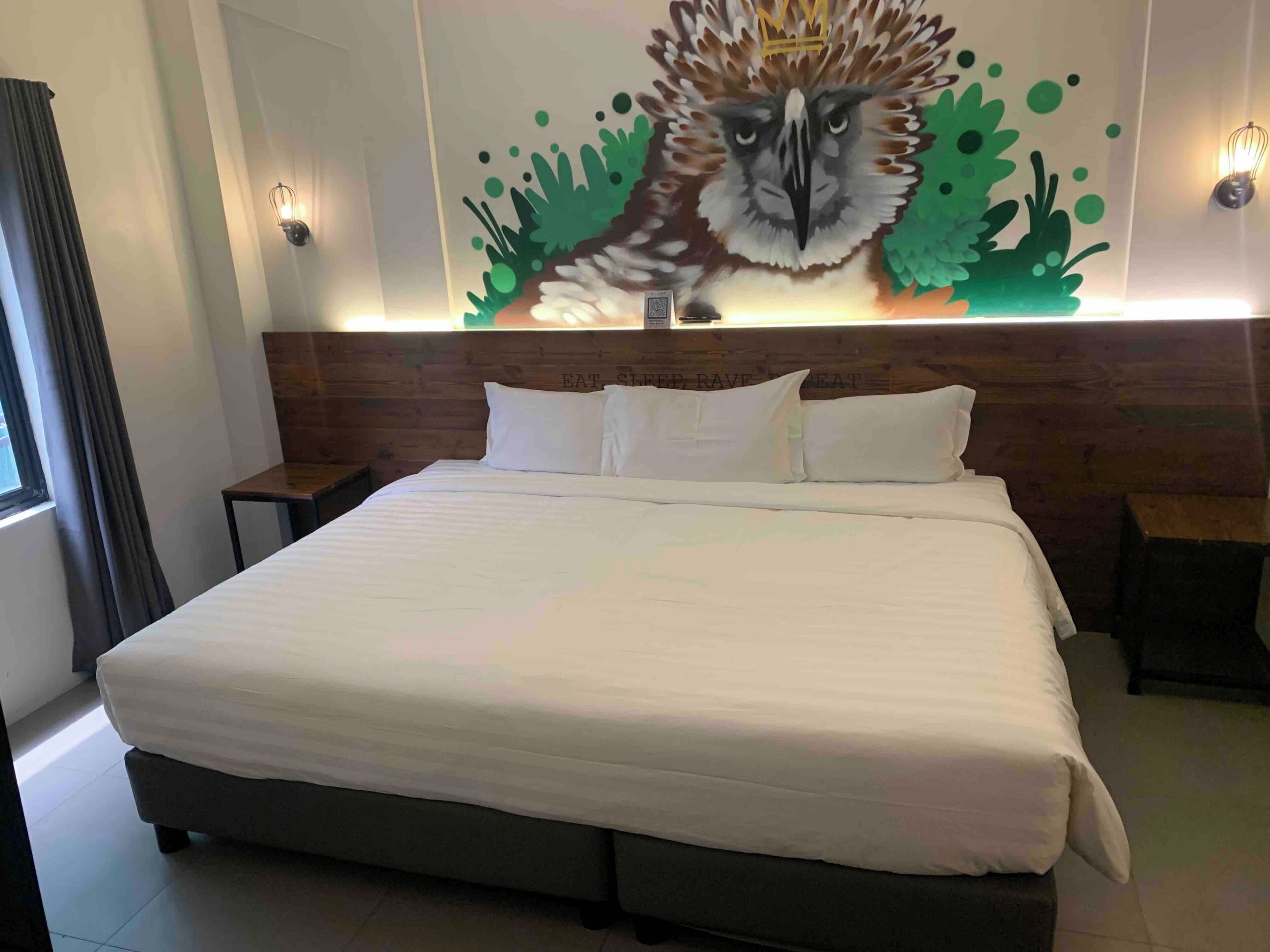 Une chambre d’hôtel avec un grand lit, une tête de lit en bois et une fresque murale représentant un animal.