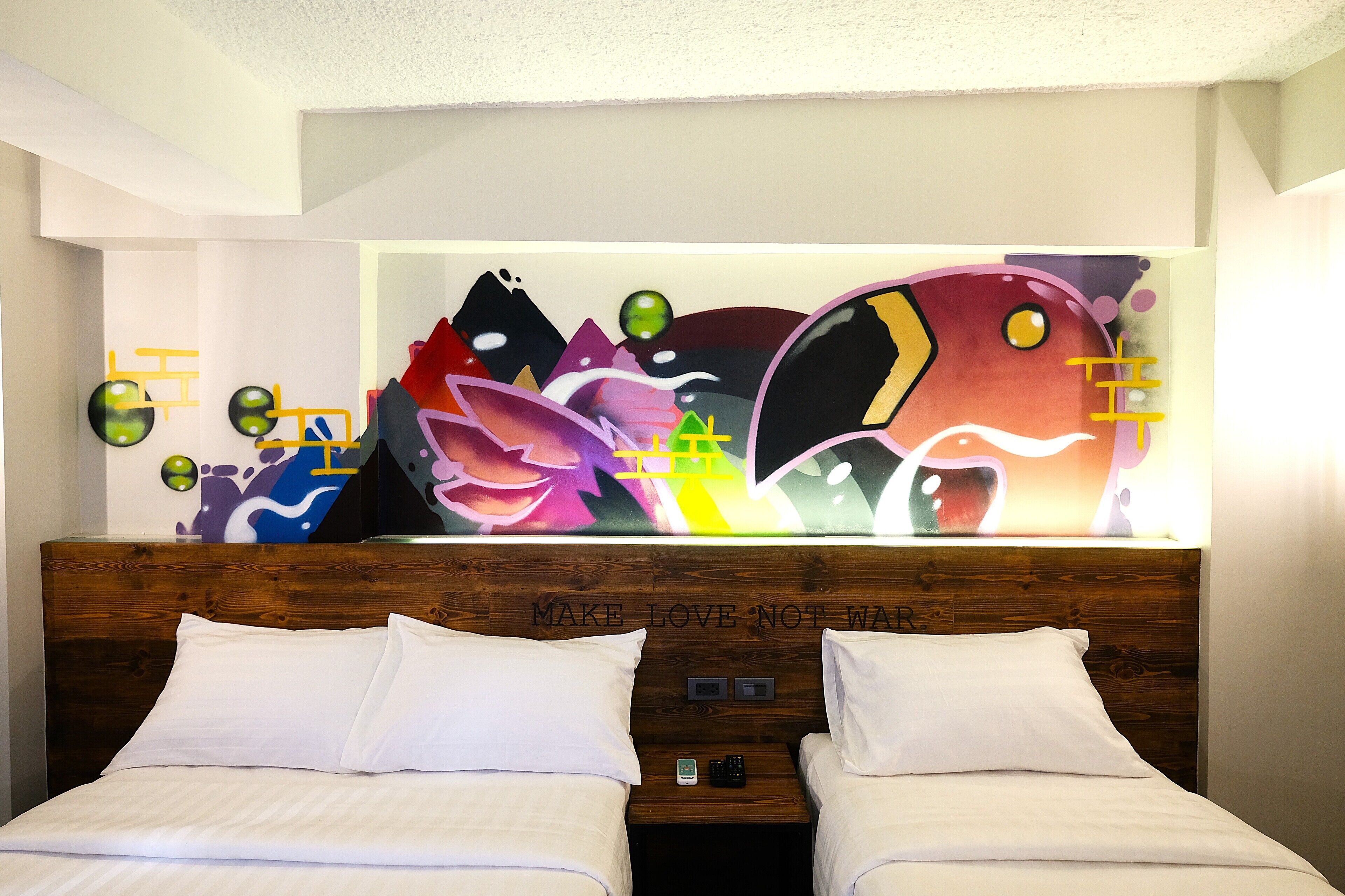 Une chambre d’hôtel avec deux lits, une tête de lit en bois et une fresque murale abstraite et colorée.