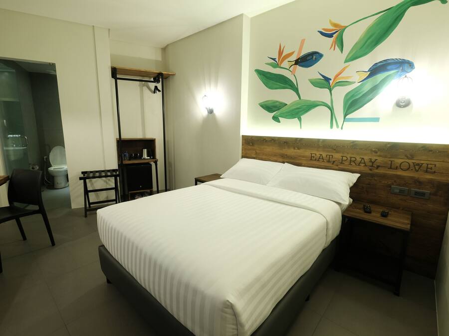 Una habitación de hotel con cama, escritorio, silla, mesita de noche y una obra de arte en la pared.