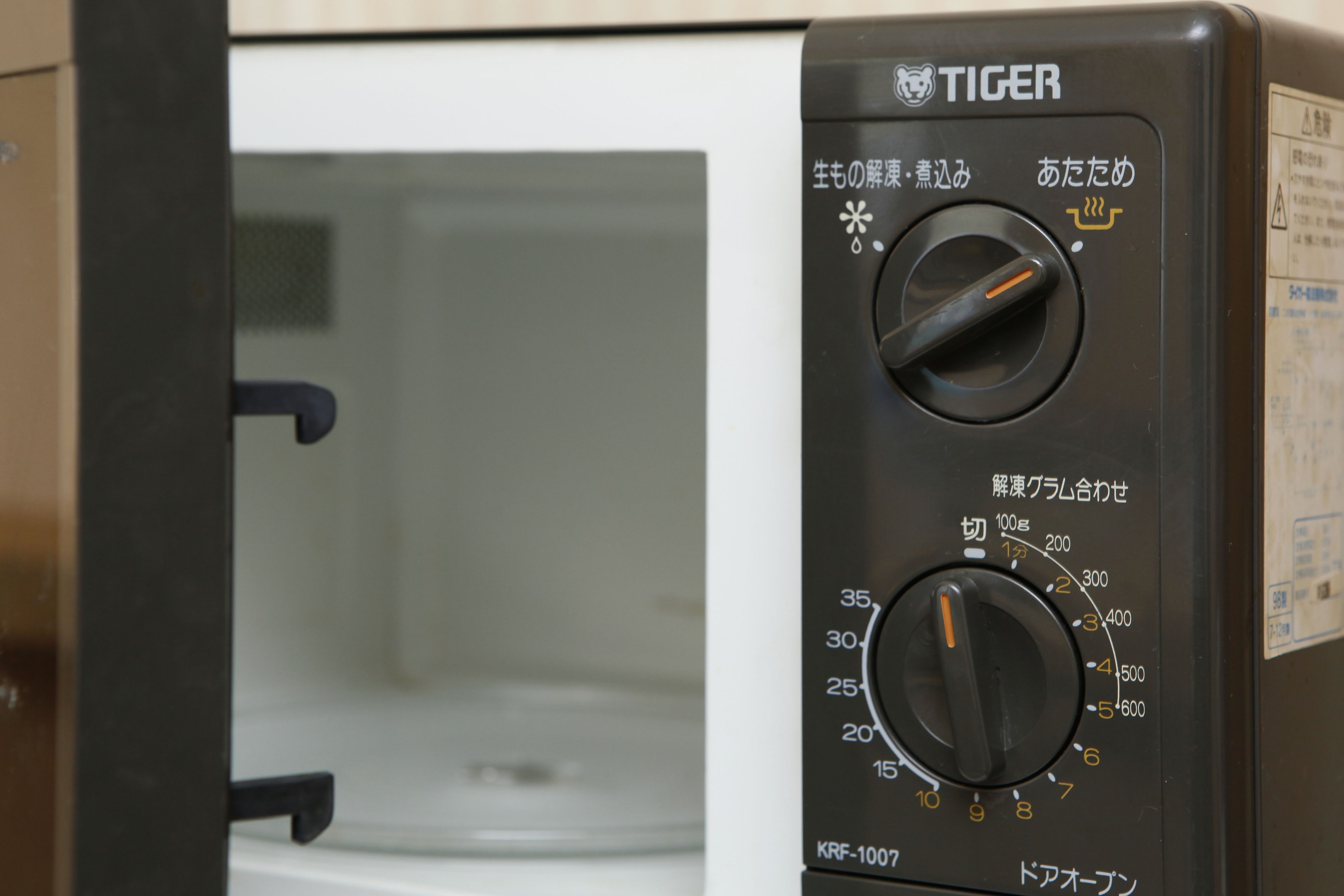 Un four à micro-ondes doté de deux boutons de réglage et d’inscriptions en japonais.