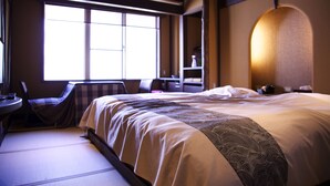 A hotel room with a large bed, a desk, and a chair. There is a window providing natural light and a view of the outside. - Nakaya Ryokan (Minakami)