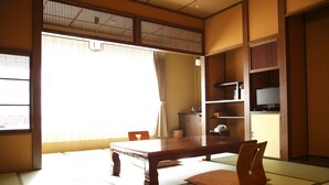A traditional Japanese room with tatami flooring, a wooden dining table, and a television on a shelf. - Nakaya Ryokan (Minakami)
