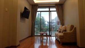 Uma sala de estar com um sofá, uma mesinha e uma TV fixada na parede.