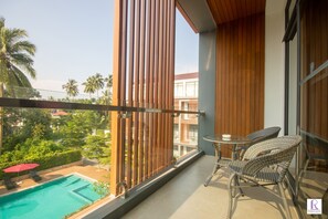 Uma varanda com cadeiras de vime e uma pequena mesa, com vista para uma piscina e palmeiras.