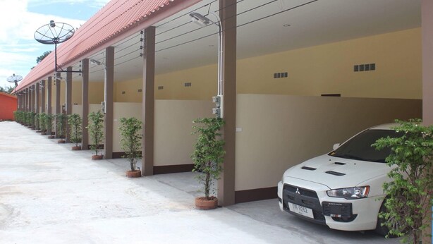 A row of covered parking spaces with potted plants, a white car parked in one space, and satellite dishes on the roof. - Rim Khuan Resort (Khuan Khanun)