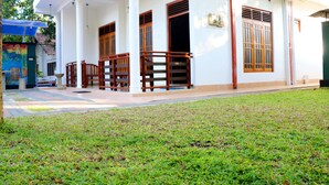 A building with a covered porch, wooden railings, and a well-maintained lawn. - The cool nest yala hotel (Thissamaharama)