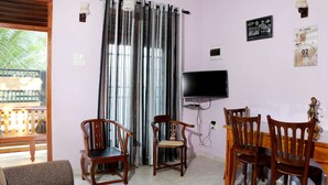 A living room with a sofa, wooden chairs, a dining table, a TV, and a large window with curtains. - The cool nest yala hotel (Thissamaharama)