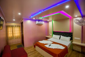 A hotel room with a bed, a bedside table, a fan, and an air conditioning unit. - Jct Houseboats (Ambalapuzha)