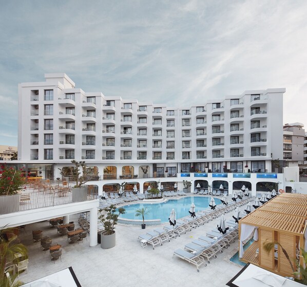 Un hotel con una piscina exterior grande, varios balcones y zonas de estar al aire libre.