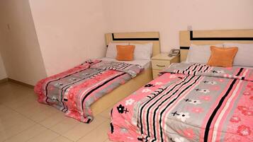 Dos camas individuales con ropa de cama floral, una mesita de noche con lámpara y un teléfono en la pared.