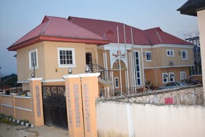 A two-story building with a red roof, a gated entrance, and a sign for 'Briggs & Hotel and Suites'. - Buggatti Hotel and Suites (Port Harcourt)