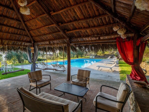 A covered outdoor area with a pool, lounge chairs, and a swing set.