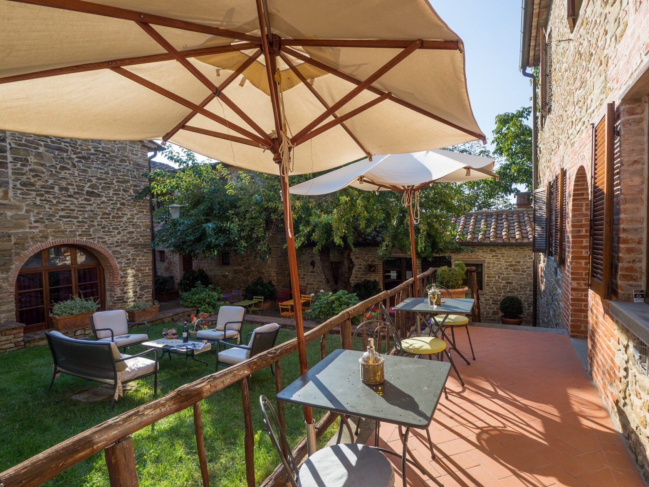 Un patio con muros de piedra, mobiliario exterior y un gran paraguas que da sombra.