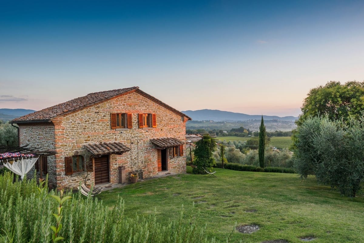 A stone house with a tiled roof, a small garden, and a view of distant hills.