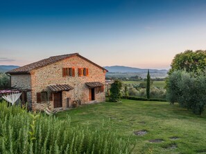A stone house with a tiled roof, a small garden, and a view of distant hills.