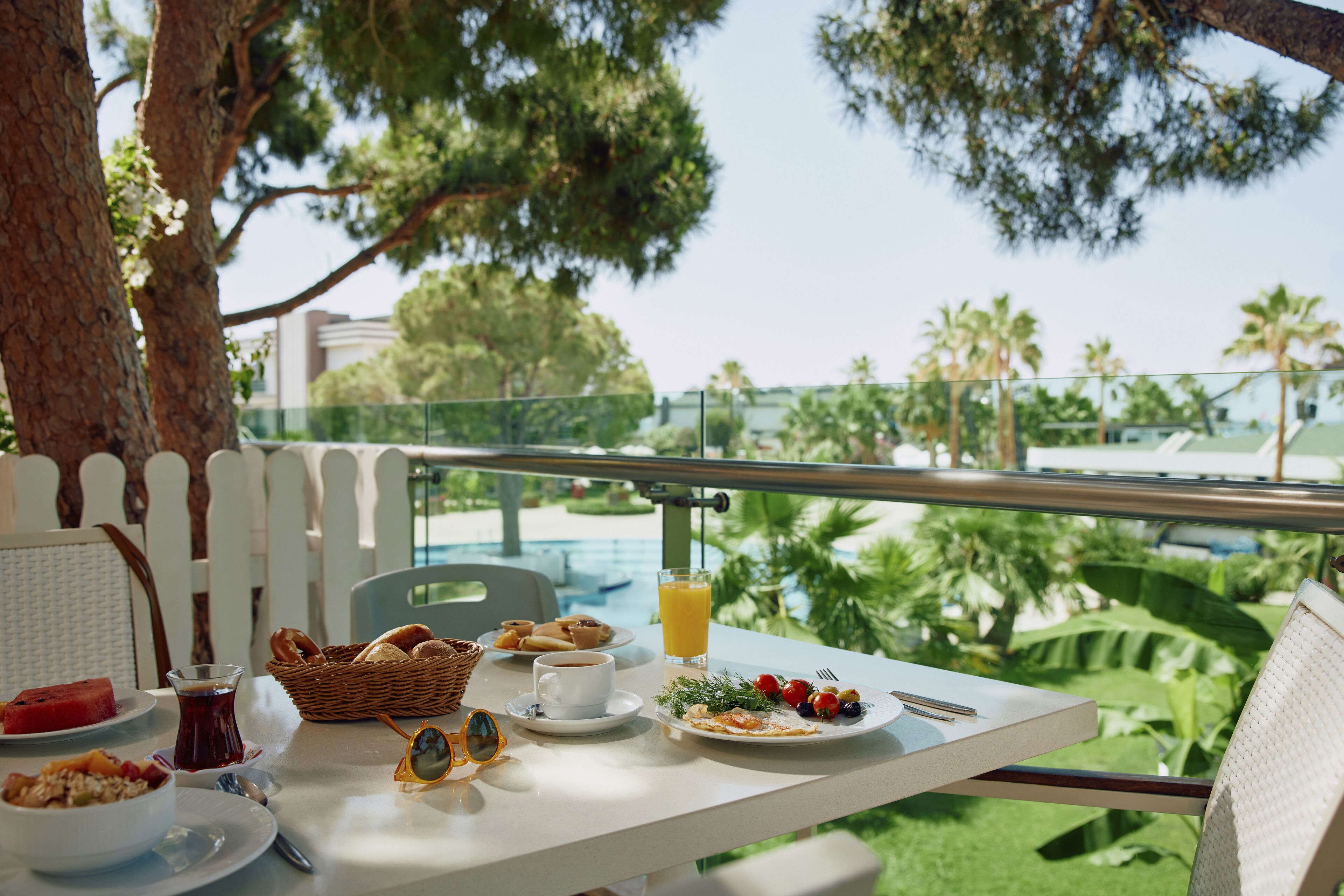 A dining table with breakfast items, a glass of orange juice, and a view of a pool and greenery.