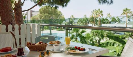 A dining table with breakfast items, a glass of orange juice, and a view of a pool and greenery.