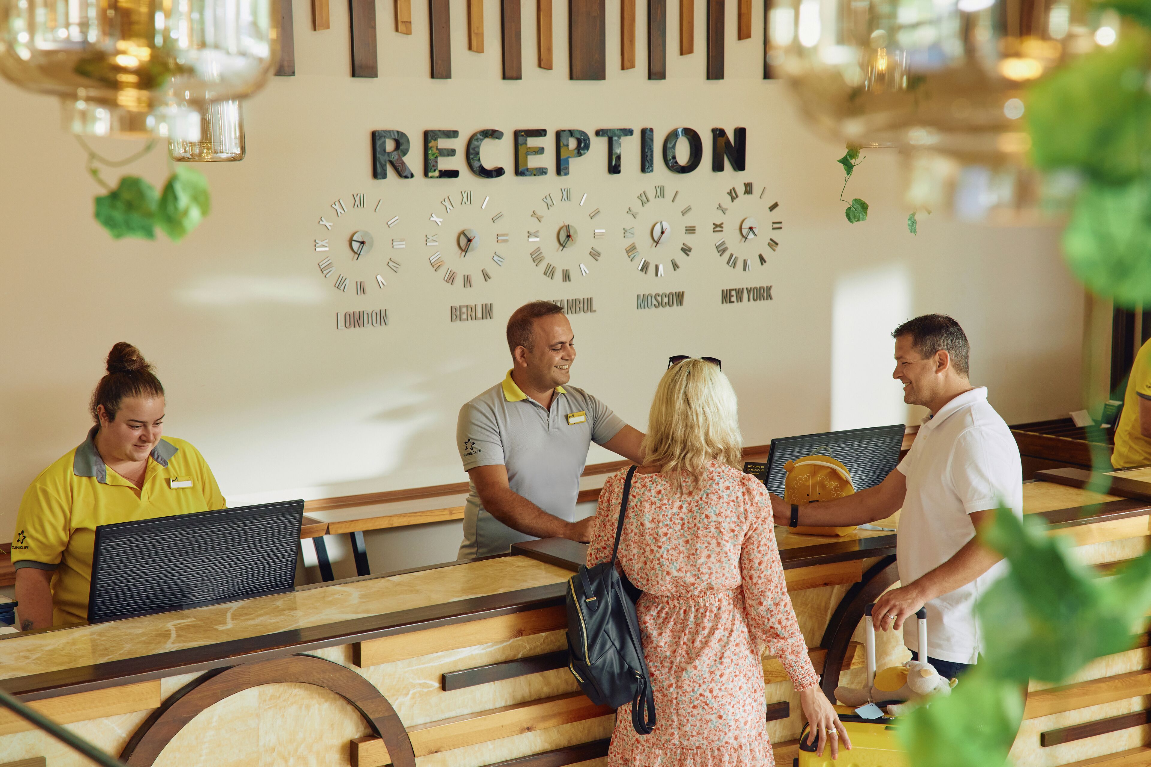 A reception desk with clocks displaying times from various cities, a wooden reception area, and a name tag on the staff member's shirt.
