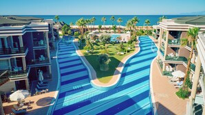 A resort with a large swimming pool, palm trees, and a view of the ocean. - TUI MAGIC LIFE Masmavi - All inclusive (Serik)