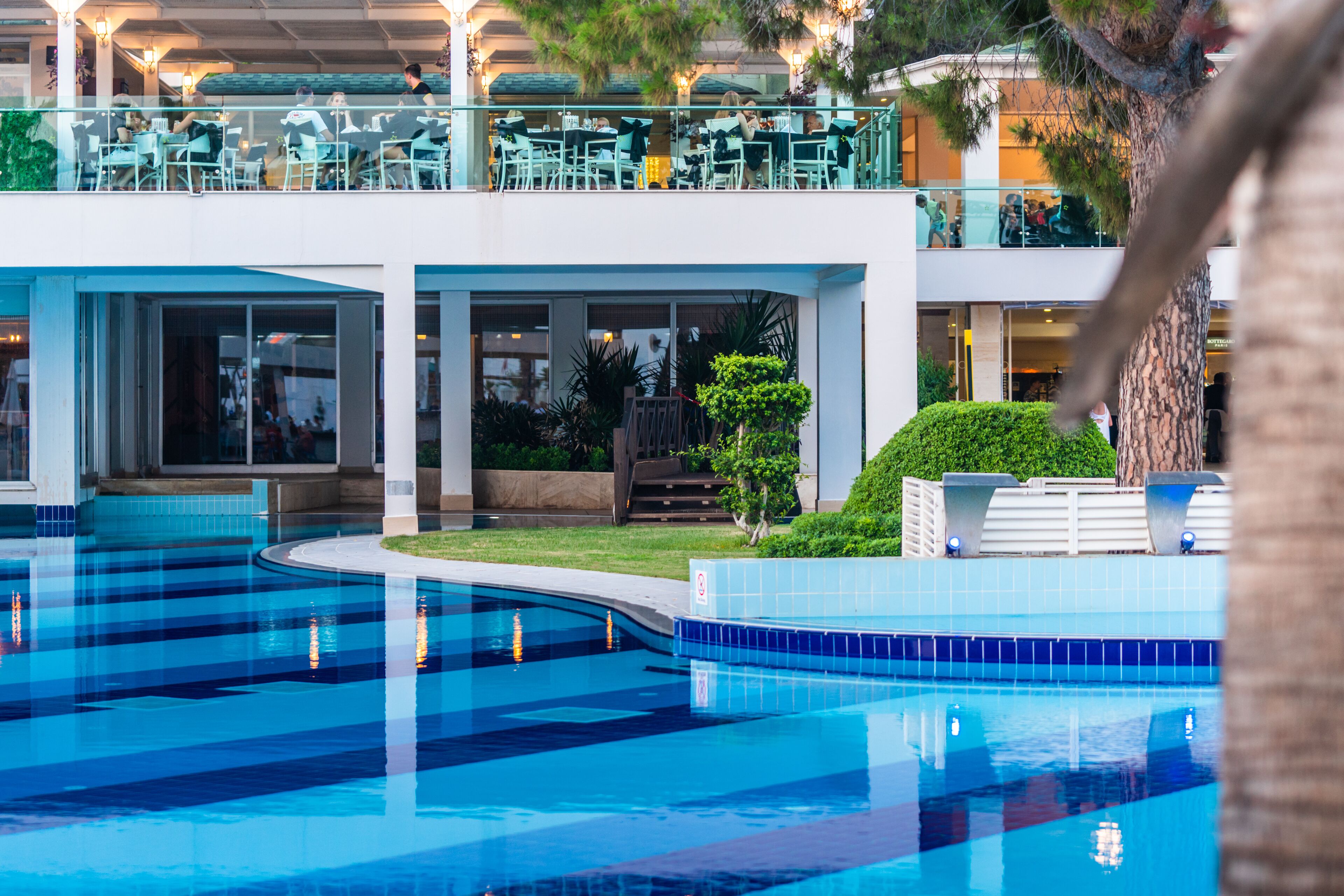 A pool area with a clear blue pool, a second-floor balcony with outdoor seating, and a well-maintained garden.