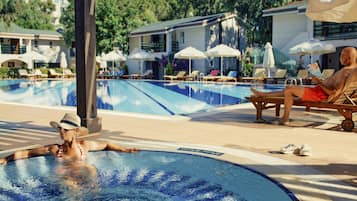 Una piscina con sillas de descanso y sombrillas, rodeada de edificios y vegetación.