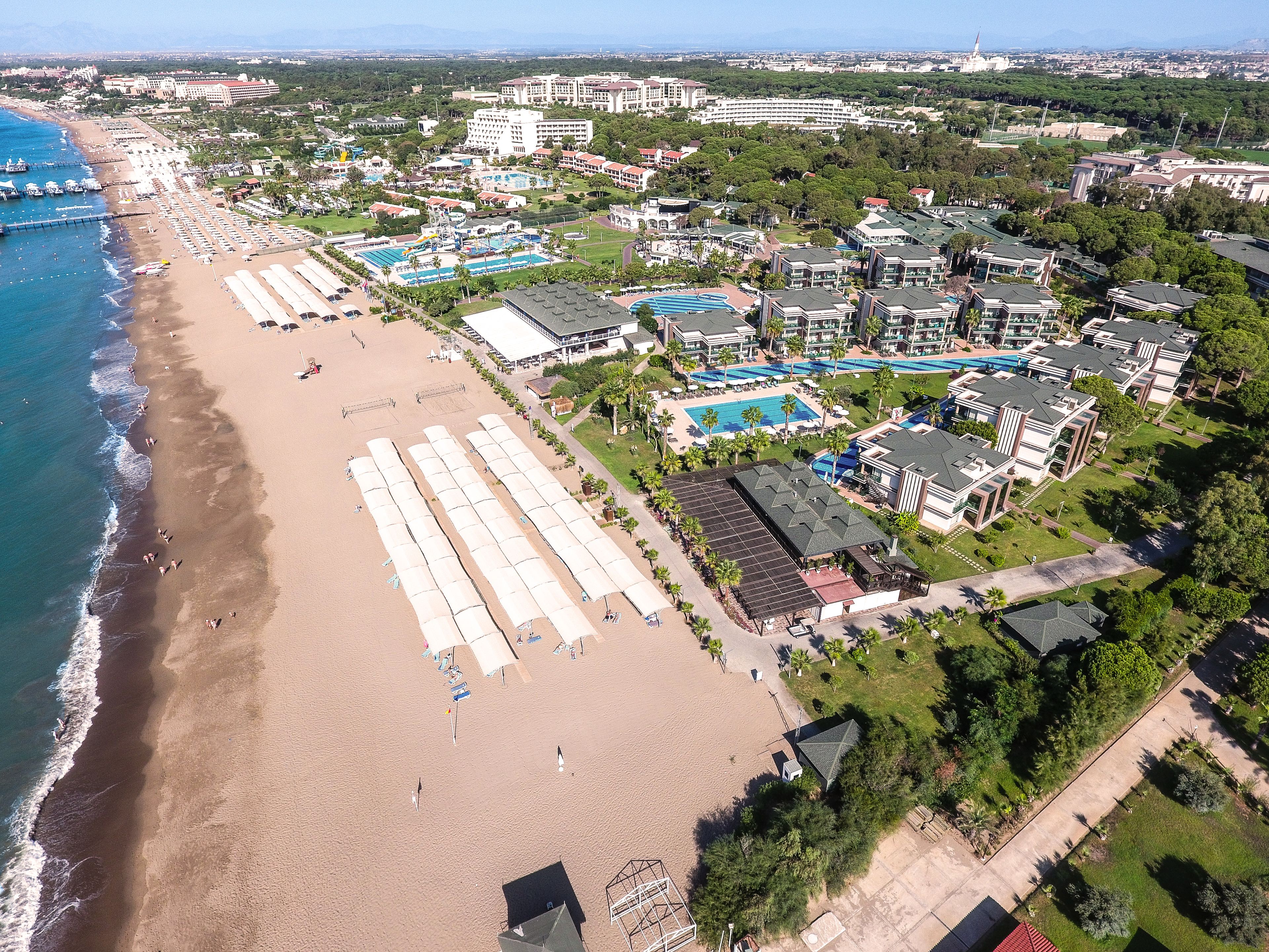Vista aérea de un complejo turístico costero con playa, múltiples piscinas y una variedad de edificios.