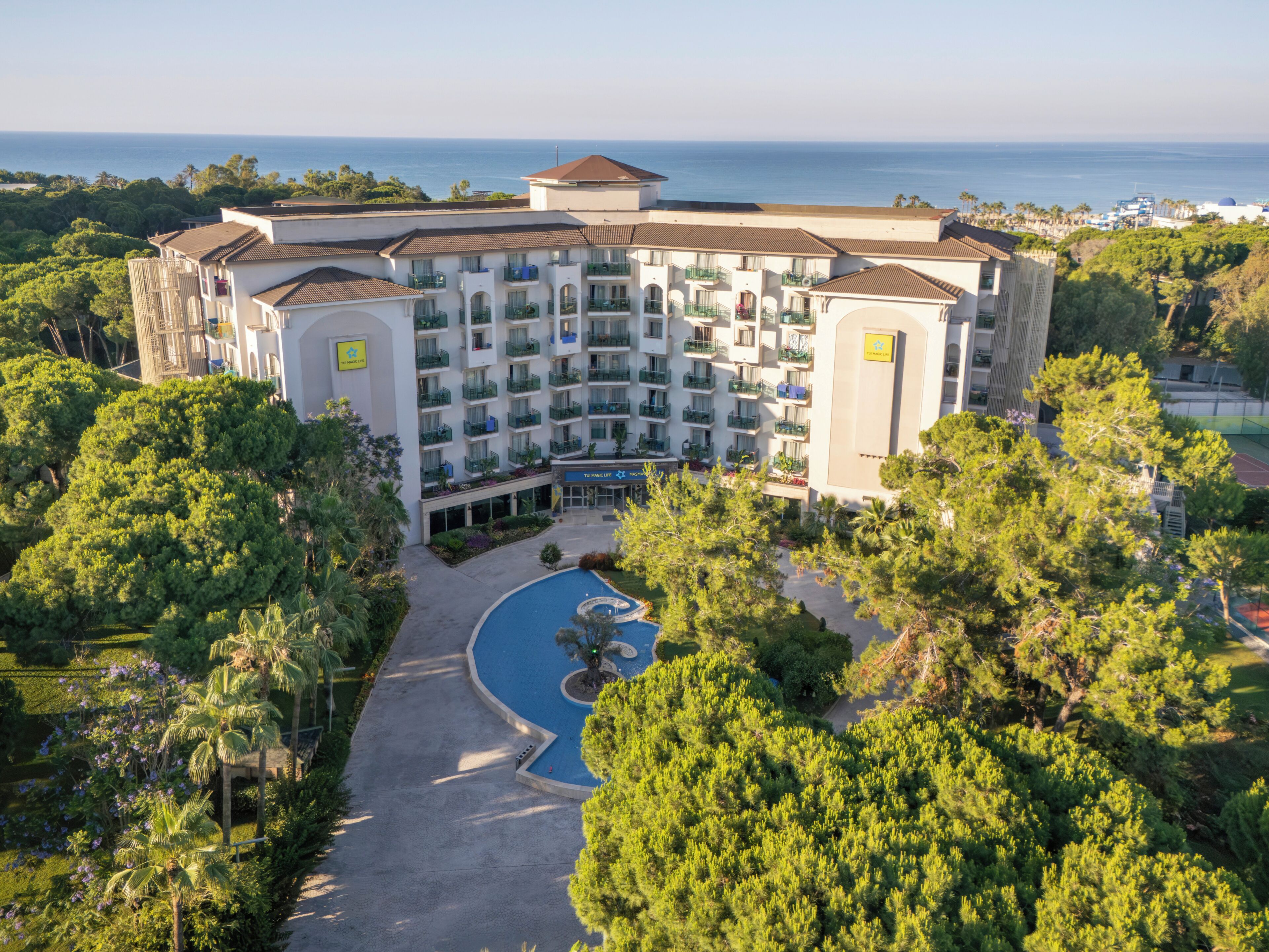 Un hotel de varios pisos con piscina, rodeado de exuberante vegetación y vistas al mar.
