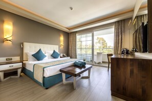 A hotel room with a large bed, bedside tables, a wooden bench, a desk, a TV, and a balcony with a view.