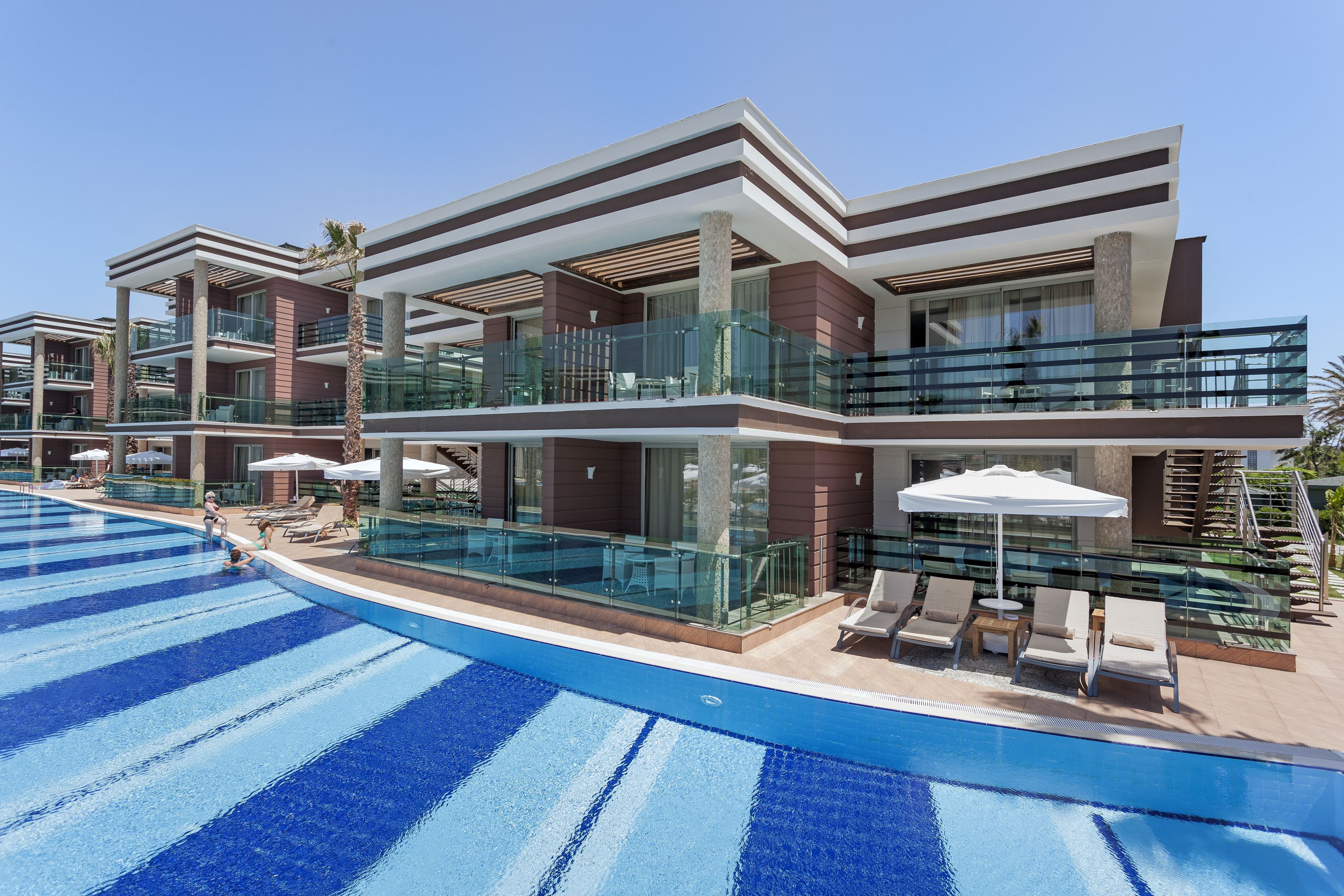 Un hotel moderno con piscina, barandas de vidrio y zonas de estar al aire libre.