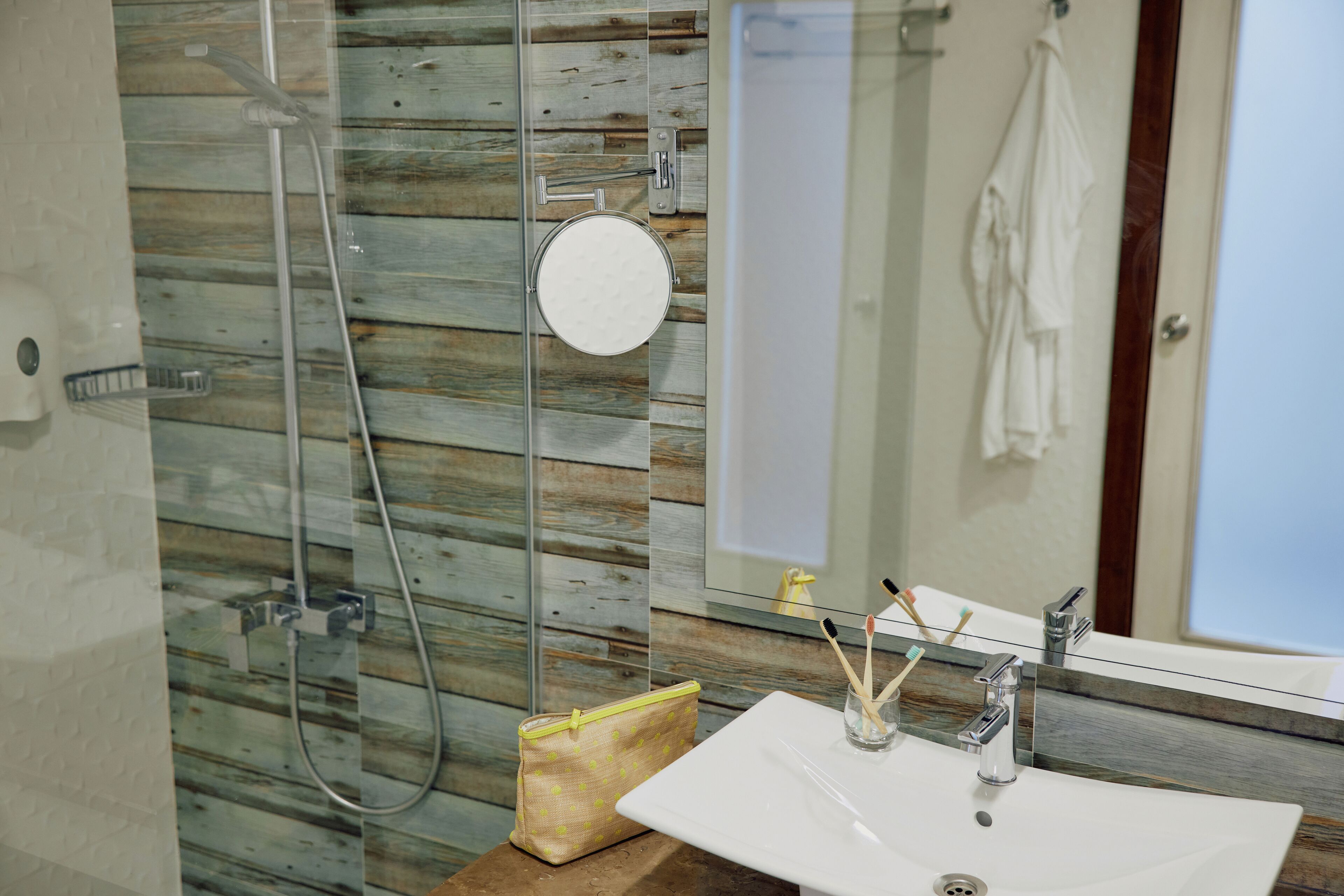A bathroom with a glass shower enclosure, a white sink with a mirror above it, and a towel hanging on the wall.