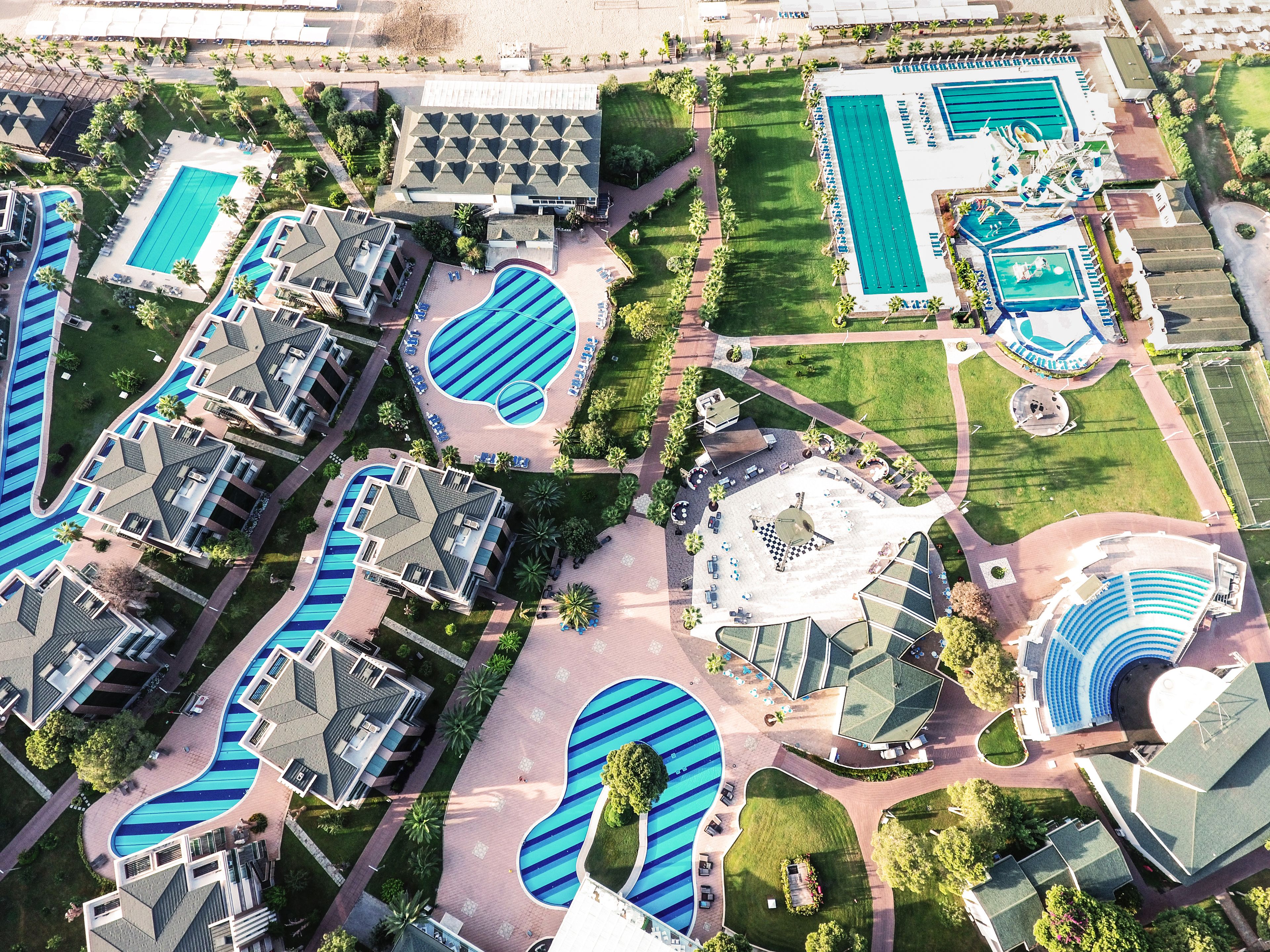 An aerial view of a resort with multiple swimming pools, a central plaza, and surrounding buildings.
