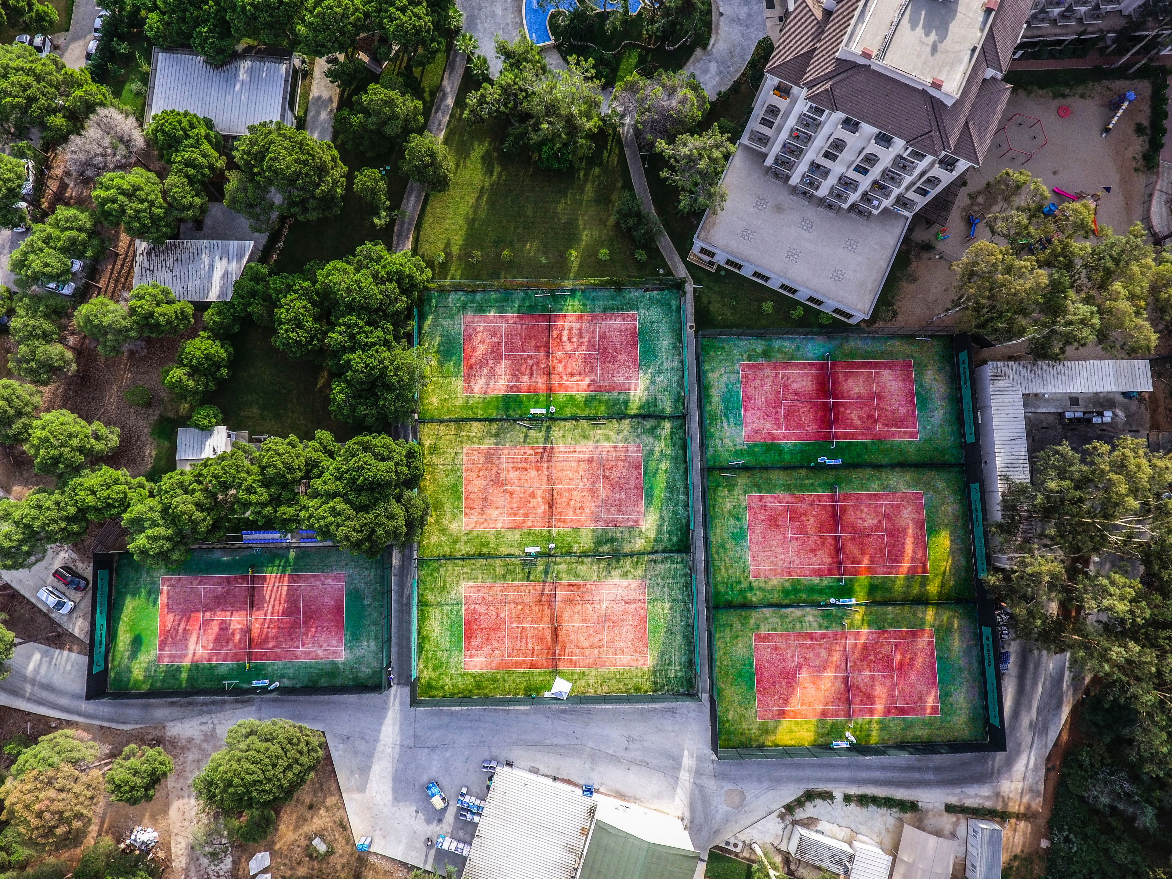 An aerial view of a residential area with multiple tennis courts, surrounded by trees and houses.