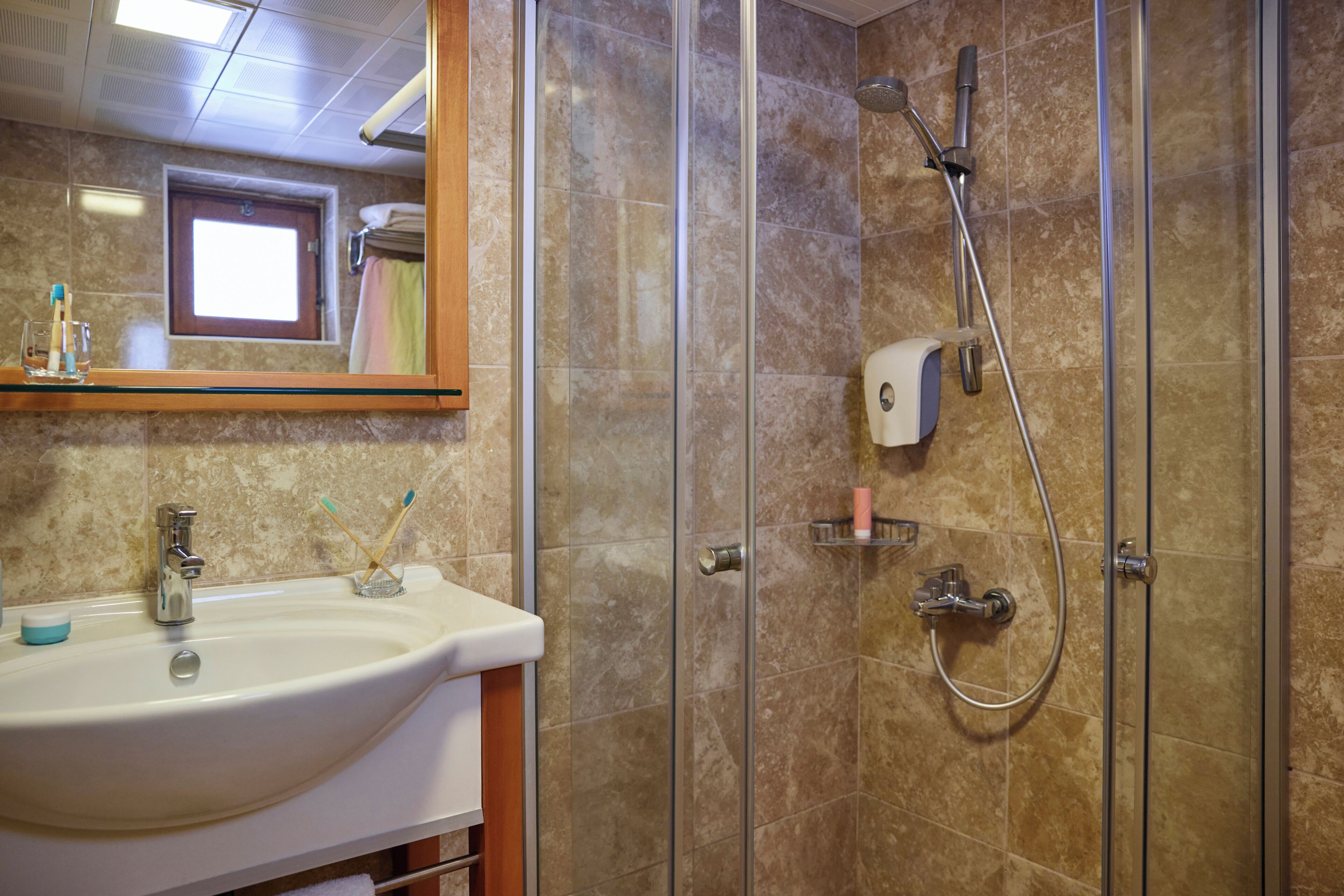 Baño con lavamanos, espejo, ducha y artículos de aseo.