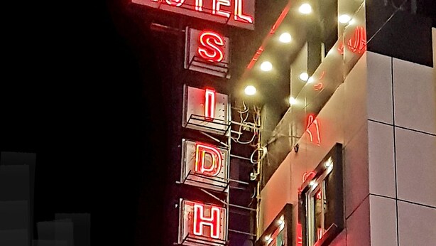 Un hotel con insegne al neon che riportano il suo nome e un cartello per un albergo turistico sottostante.