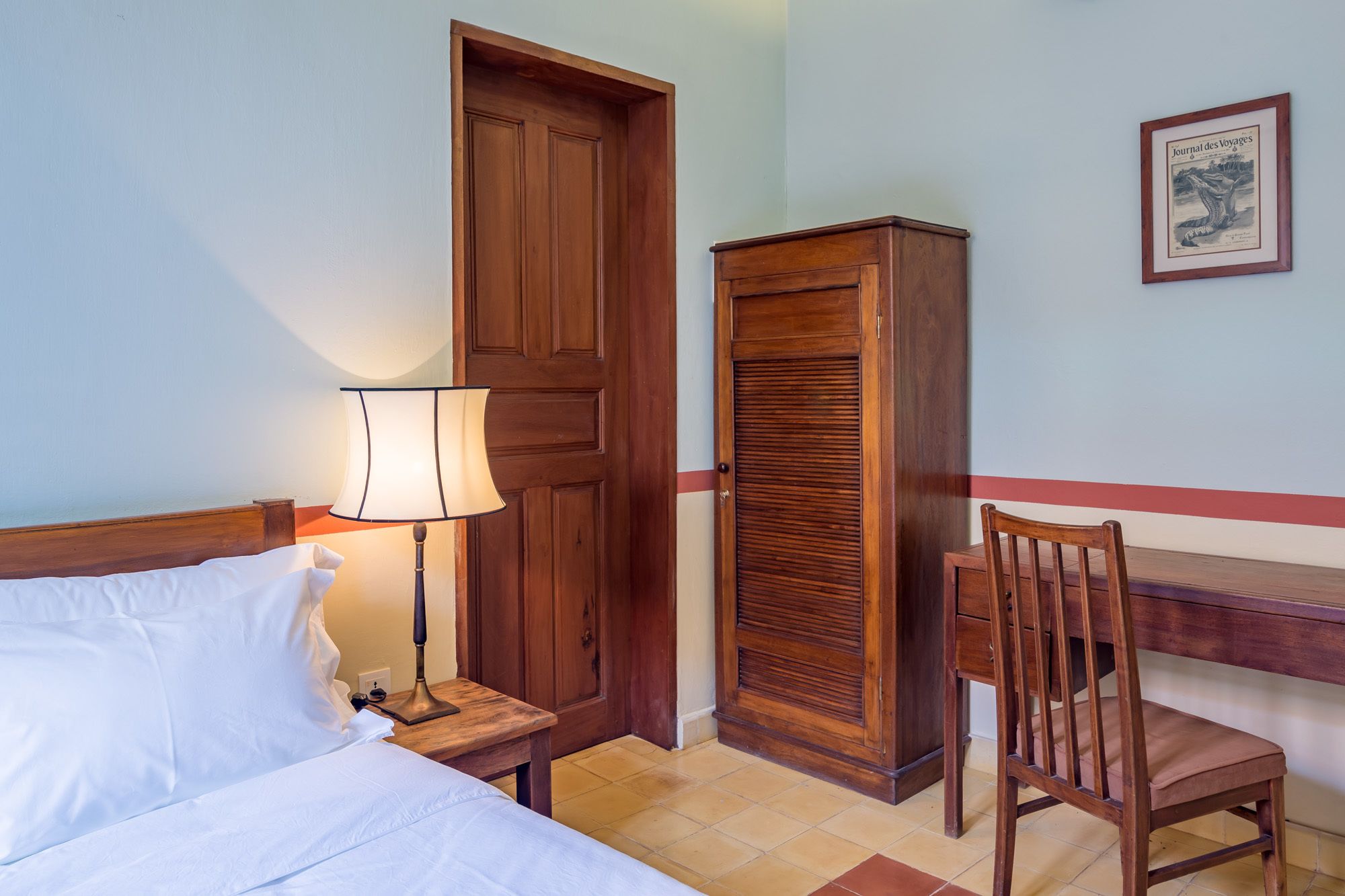 Una habitación de hotel con cama, escritorio, silla, armario y lámpara.